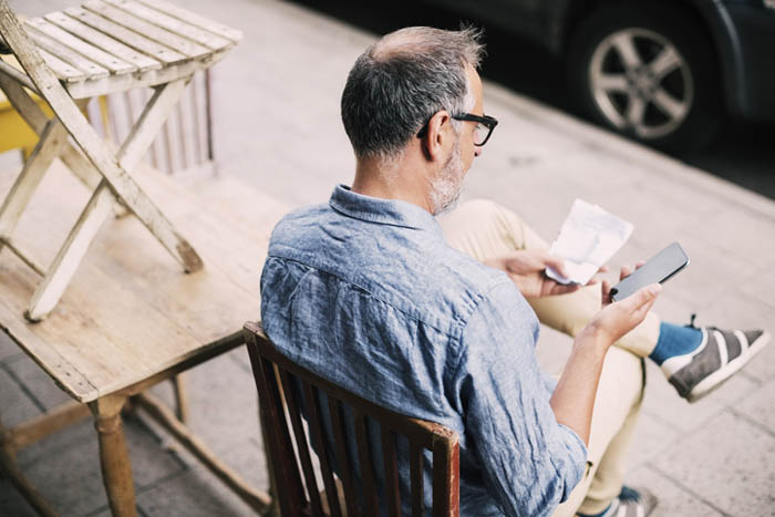 High angle view of man using mobile phone while sitting on chair Mand sidder på en fortovscafé og kontakter Trollecare på telefon