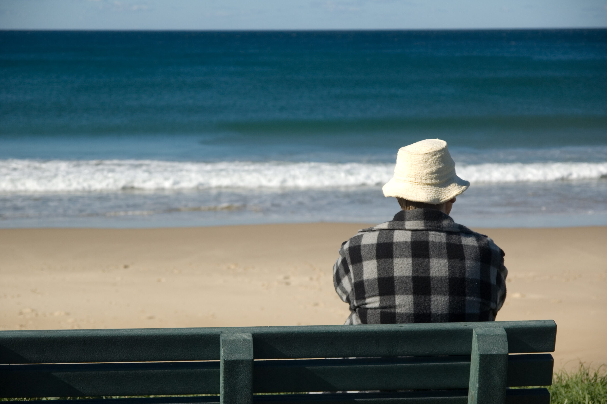 Man sitting on a beach bench looking at sand and water